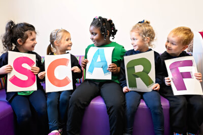 Pupils sitting down looking at one another, each holding a letter that spells SCARF