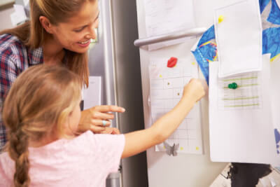 Photograph of parent or carer and child putting a list onto a fridge