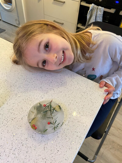 Photograph of Eloise and her frozen sun catcher with green leaves and red berries.