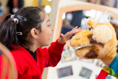 photograph of child stroking giraffe puppet and both smiling