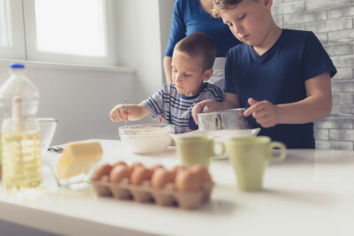 Mother with two primary-age sons, baking together, with cake-making ingredients and measuring tools